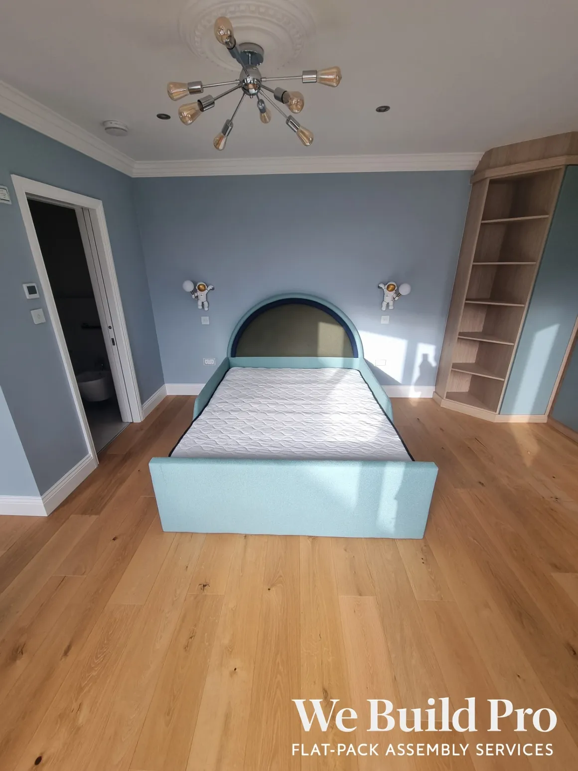 Children's bedroom with turquoise bed, built-in shelving, and modern chandelier