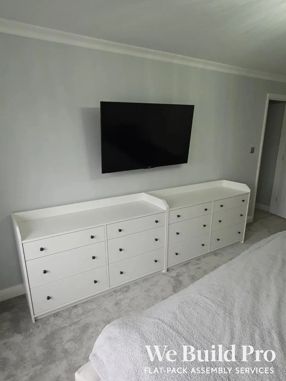 White built-in storage units with multiple drawers under wall-mounted TV