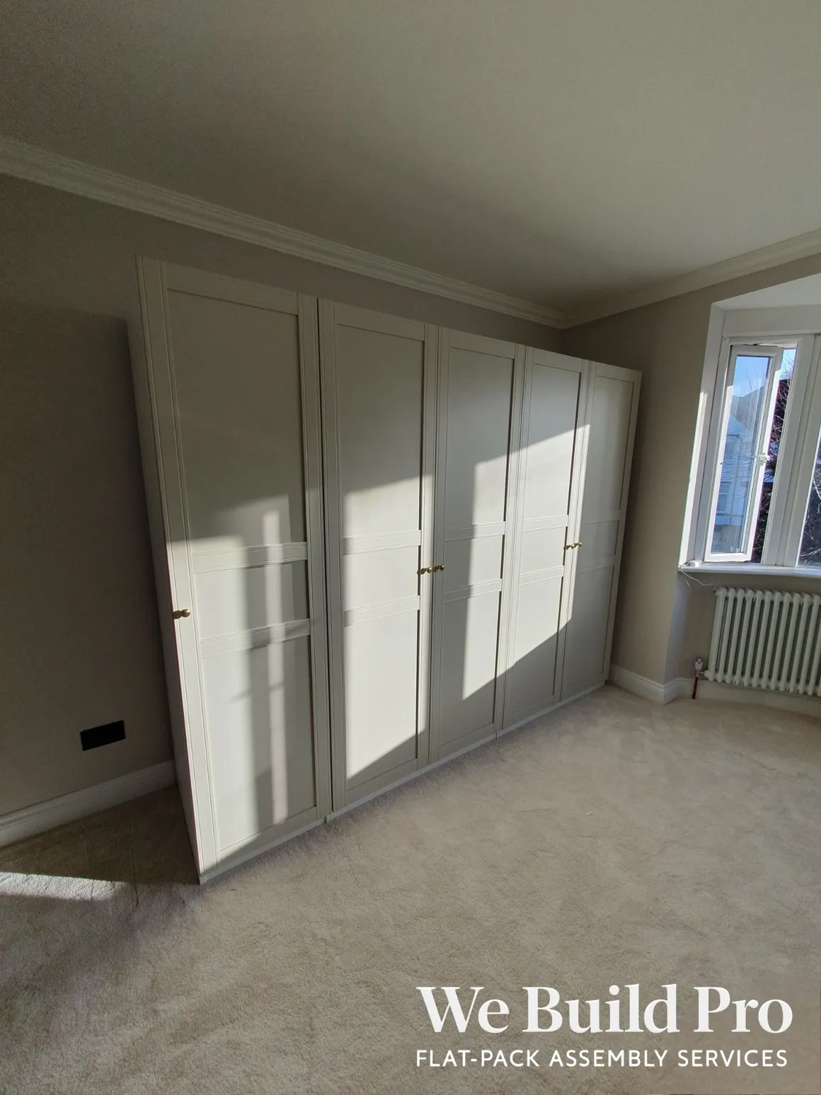 White built-in wardrobes with panel doors and brass handles in bedroom