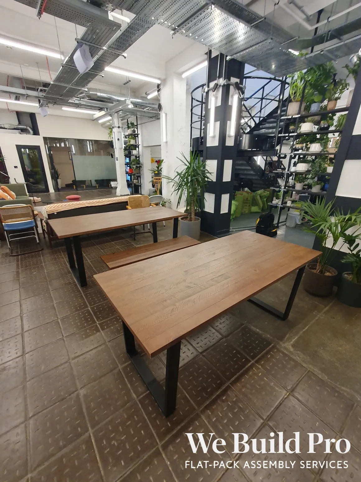 Industrial coworking space with wooden tables, spiral staircase and plants